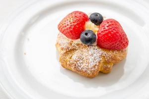 close-up van Deens gebak vers fruit, verse croissant met slagroom en aardbeien bosbessen op een witte plaat foto