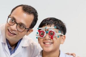 glimlachende indische jongen die een bril kiest in een optiekwinkel, een jongen die een oogtest doet die onderzoek controleert met een optometrist met behulp van een proefframe in een optische winkel foto
