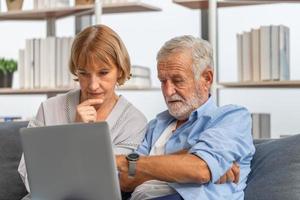 bezorgd senior paar hun rekeningen controleren en werken op netbook documentinformatie thuis lezen, gepensioneerde bejaarde oude familie documenten lezen met laptop foto