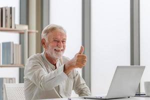 portret van senior man met laptop met laptop pratend over videogesprek thuis, gelukkige senior man in woonkamer met laptopcomputergadget foto