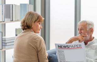 portret van senior koppel in woonkamer, oudere vrouw en een man die een krant leest op een gezellige bank thuis, familieconcepten foto