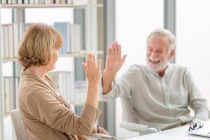 gelukkig senior koppel in de woonkamer, glimlachend ouder koppel dat high five geeft, geluksfamilie en pensioenconcepten foto