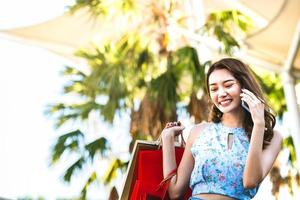 Aziatische positieve vrouw die vrienden belt tijdens het winkelen foto