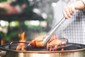 man hand met tang grillen barbecue in brand in achtertuin op dag. foto