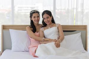 een Aziatische bruid in een witte trouwjurk met haar vrienden liggend op het bed glimlachte samen. foto