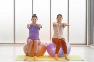twee Aziatische vrouwen van middelbare leeftijd doen yoga zittend op een rubberen bal in de sportschool. foto