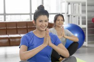 twee Aziatische vrouwen van middelbare leeftijd doen yoga op een rubberen mat in haar huis. foto