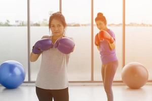 twee aziatische vrouwen van middelbare leeftijd doen boksoefeningen in de sportschool en hebben een lichtoranje achtergrond. foto