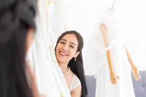 een aziatische bruid kiest een jurk voor haar bruiloft en staat vrolijk te glimlachen voor de vrienden die samenkomen. foto