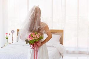 een Aziatische bruid droeg een witte trouwjurk, staand, met een boeket prachtige bloemen achter zich. foto
