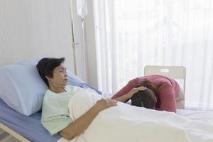 een zieke moeder in bed, Aziatische vrouw wreef over het hoofd van haar dochter in slaap in het ziekenhuisbed foto