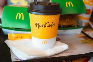 een papieren kopje mcdonald's koffie met het opschrift maccafe in het russisch en een hamburger in een doos op een dienblad. fastfoodrestaurantketens. Rusland, Kaluga, 21 maart 2022. foto