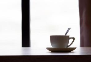 koffie in witte kop op houten tafel in café met verlichtingsachtergrond foto