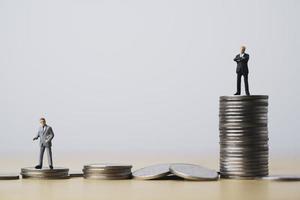 miniatuurfiguur van twee zakenlieden die staan voor verschillende hoge en lage munten die stapelen voor positie en succesvol bedrijfsinvesteringsinkomstenconcept. foto