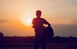 het silhouet van een gitarist die een gitaar vasthoudt en een zonsondergang heeft, silhouetconcept. foto