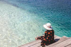 vrouwen toerist in zomerhoed met smartphone op houten bankje boven de zee bij labuan bajo foto