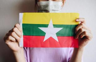 bijgesneden opname van een vrouw die een masker draagt en de vlag van myanmar toont tijdens de covid-19-pandemie. foto