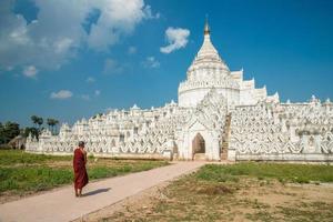 Birmese monnik die voor de hsinbyume-pagode staat, andere naam genaamd 'taj mahal van de irrawaddy-rivier'. deze pagode die de berg meru van de boeddhistische kosmologie vertegenwoordigt, gelegen in de sagaing-regio van myanmar. foto