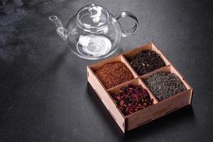 verschillende soorten droge zwarte thee met bergamot, rooibos, groen en frame in een houten kist op een zwarte betonnen ondergrond foto