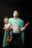 vader met een medisch masker houdt zijn dochtertje vast. het concept om kinderen te beschermen tijdens de epidemie van coronavirus foto