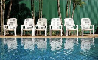 lege witte plastic stoelen bij blauw zwembad in hotelresort. foto