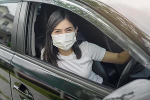 jonge mooie vrouw die een beschermend masker draagt dat een auto bestuurt foto