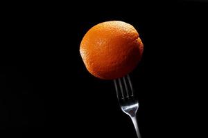 close-up van vers oranje fruit op een vork op zwarte achtergrond gewichtsverlies dieet gezond voedsel concept. vers tropisch fruit, oranje citrus, ruimte voor tekst. gezond dieet. gewichtscontrole. foto