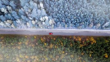 de grens van herfst en winter. auto rijdt op de weg in het bos bovenaanzicht van de drone. foto