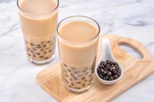 populaire taiwan-drank - bubbelmelkthee met tapioca-parelbal in drinkglas op marmeren witte tafel houten dienbladachtergrond, close-up, kopieer ruimte foto