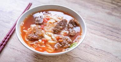 rundvlees noodle ramen maaltijd met tomatensaus bouillon in kom op lichte houten tafel, beroemde Chinese stijl eten in Taiwan, close-up, bovenaanzicht, kopieer ruimte foto