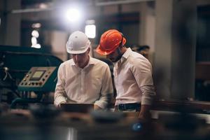 fabrieksarbeider man en ingenieur manager werken samen aan een industriële werkplaats van metaalplaat, controleren het machineproces op de laptop en dragen een veiligheidshelm foto