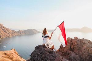 een vrouw die bovenop heuvels staat en de vlag van Indonesië vasthoudt op het eiland Labuan Bajo foto