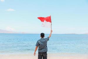 een man die op het strand staat en de Indonesische vlag zwaait met een zeegezichtachtergrond foto