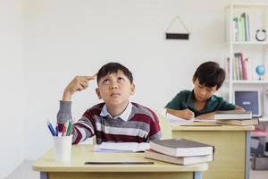 Aziatische studentenjongen die tijdens examen in een klaslokaal denkt foto