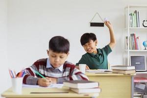 stoute schooljongen maakt grappen met zijn vriend die studeert met een papieren bal foto