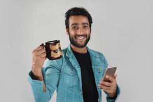 een man met een koffiekopje en mobiel die naar nieuws kijkt en lacht foto