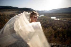 portret van een jonge mooie bruid in de bergen met een sluier. de wind vormt een sluier. huwelijksfotografie in de bergen. foto