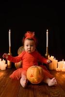 klein meisje zit op een achtergrond van jack-pompoenen en kaarsen op een zwarte achtergrond. foto