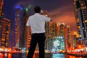 portret van een jonge knappe zakenman die op een mobiele telefoon praat en voor het stadsbeeld van luxe gebouwen staat. foto