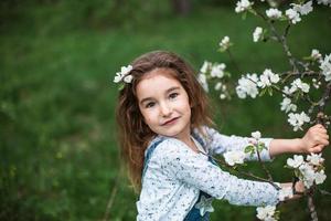 een schattig klein meisje van 5 jaar oud in een bloeiende witte appelboomgaard in het voorjaar. lente, boomgaard, bloei, allergie, lentegeur, tederheid, zorg voor de natuur. portret foto