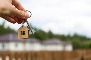 houten hanger van een huis en sleutel. achtergrond van hek en huisje. droom van huis, bouwen, ontwerp, oplevering van het project, verhuizen naar een nieuw huis, hypotheek, huur en aankoop onroerend goed. kopieer ruimte foto