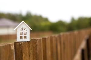 kleine figuur van wit houten huis op hek met sleutel tot huisvesting tegen de achtergrond van huisjes. bouwen, ontwerp, project, verhuizing naar nieuw huis, hypotheek, huur en aankoop onroerend goed. kopieer ruimte foto