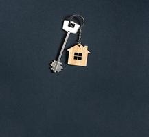 sleutelhanger in de vorm van een houten huis met sleutel op een zwarte achtergrond. bouwen, ontwerp, project, verhuizing naar nieuwe woning, hypotheek, huur en aankoop onroerend goed. kopieer ruimte foto