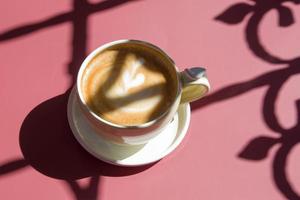 keramische kop met cappuccino met een hart versierd op schuimrubber in harde schaduwen op een gekleurde achtergrond. foto