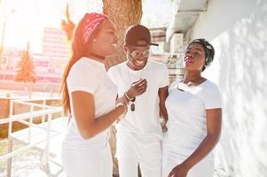 drie stijlvolle vrolijke Afro-Amerikaanse vrienden, draag witte kleren. straatmode van jonge zwarte mensen. zwarte man met twee Afrikaanse op de zon. foto