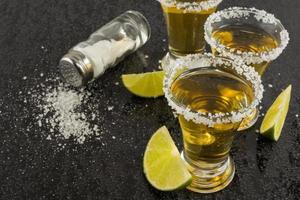 gouden tequila shots met limoen op zwarte achtergrond foto