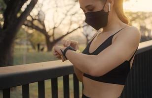 vrouw die een beschermend masker draagt en het fitness slimme horloge opzet om te rennen. sportvrouw die horlogeapparaat controleert. foto