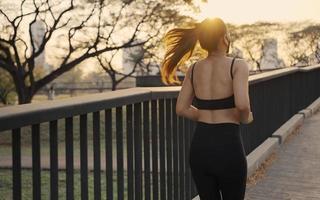 vrouw in sportkleding met een beschermend masker joggen oefening op de brug in de stad bij zonsondergang. foto