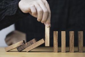 handtrek houten blok om vallende dominostenen te voorkomen en te stoppen, het is een symbool van bescherming tegen schade of stopverlies voor crisisbeheerconcept. foto