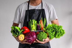 man met schort met verschillende groenten in beide handen. gezond eten en veganistisch dagconcept foto